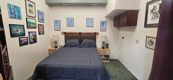 A small, neatly arranged bedroom with a bed, two bedside tables, and a wall adorned with framed artwork.