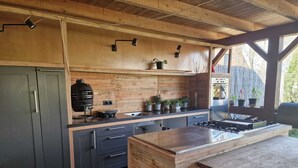 A modern kitchen with wooden cabinetry, a built-in grill, and a large island with a sink. - BoHo - Jacuzzi, Sauna, BBQ, Garden close to Amsterdam & Utrecht - Sleeps 24 (Kockengen)