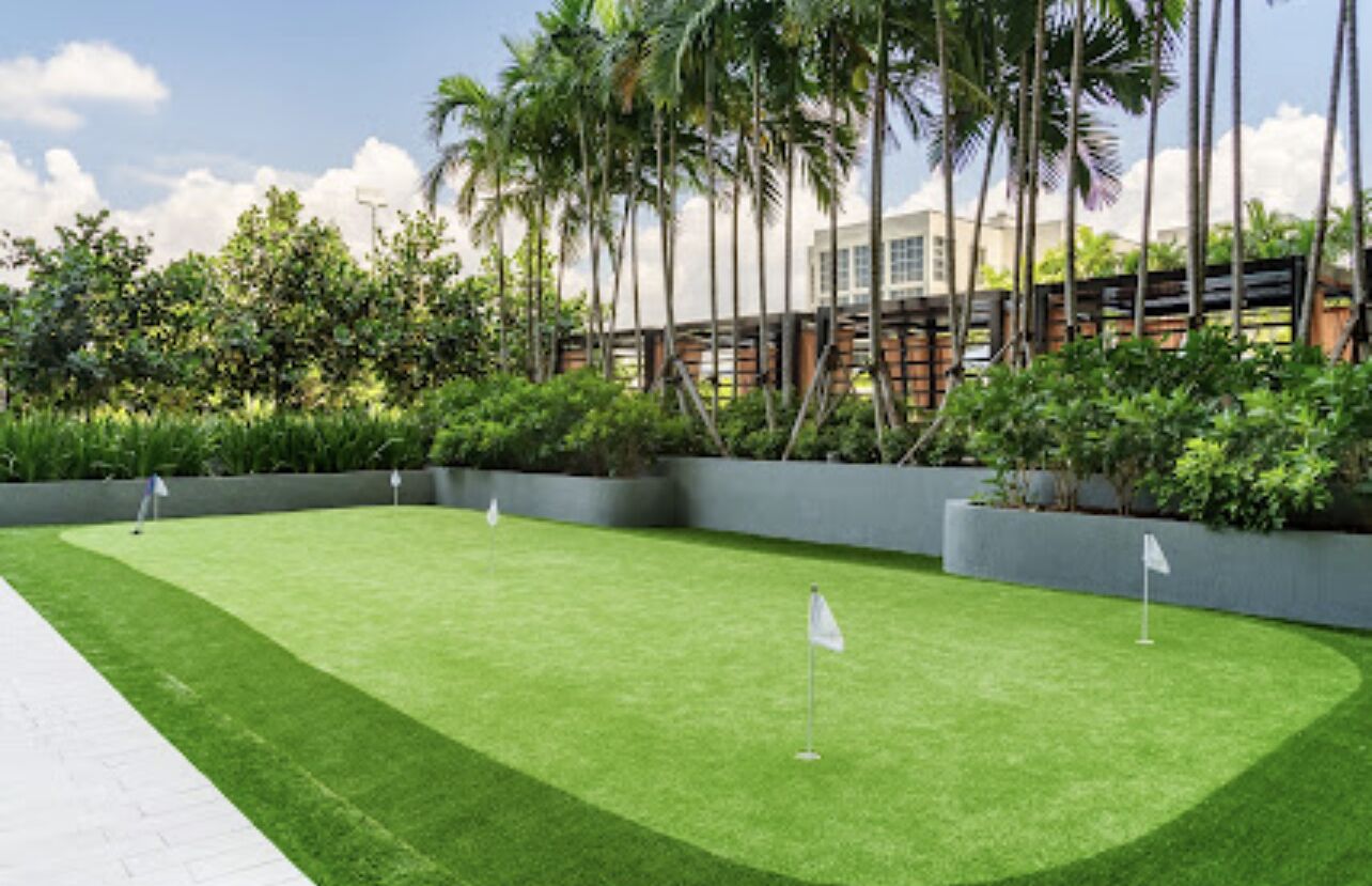 A well-maintained lawn with two flags, surrounded by lush greenery and tall palm trees.
