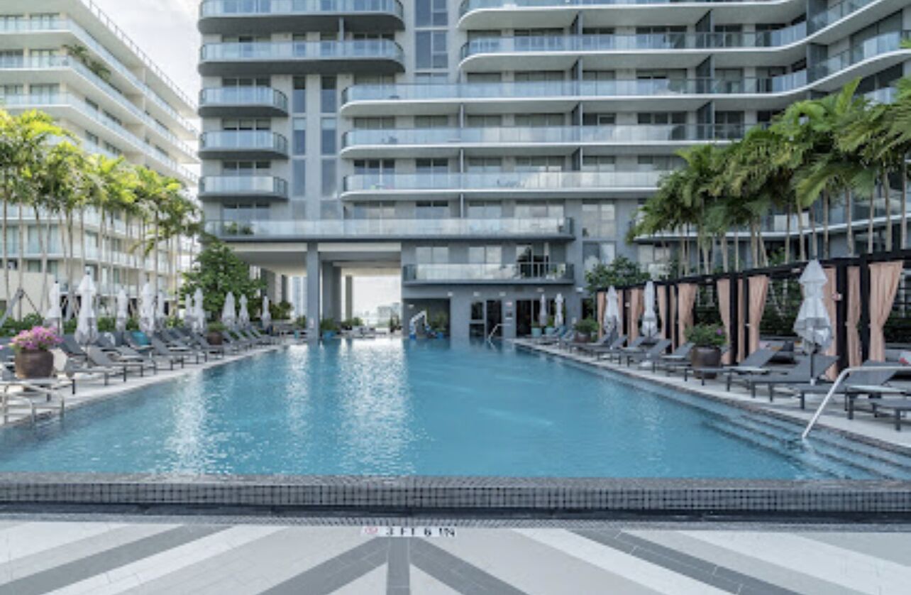 A swimming pool surrounded by lounge chairs and umbrellas, with a modern building in the background.