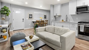 A modern living room with a sofa, coffee table, and a dining area with chairs and a table. - New Studio - Walk to Golden 1 / Old Sac / DOCO (West Sacramento)