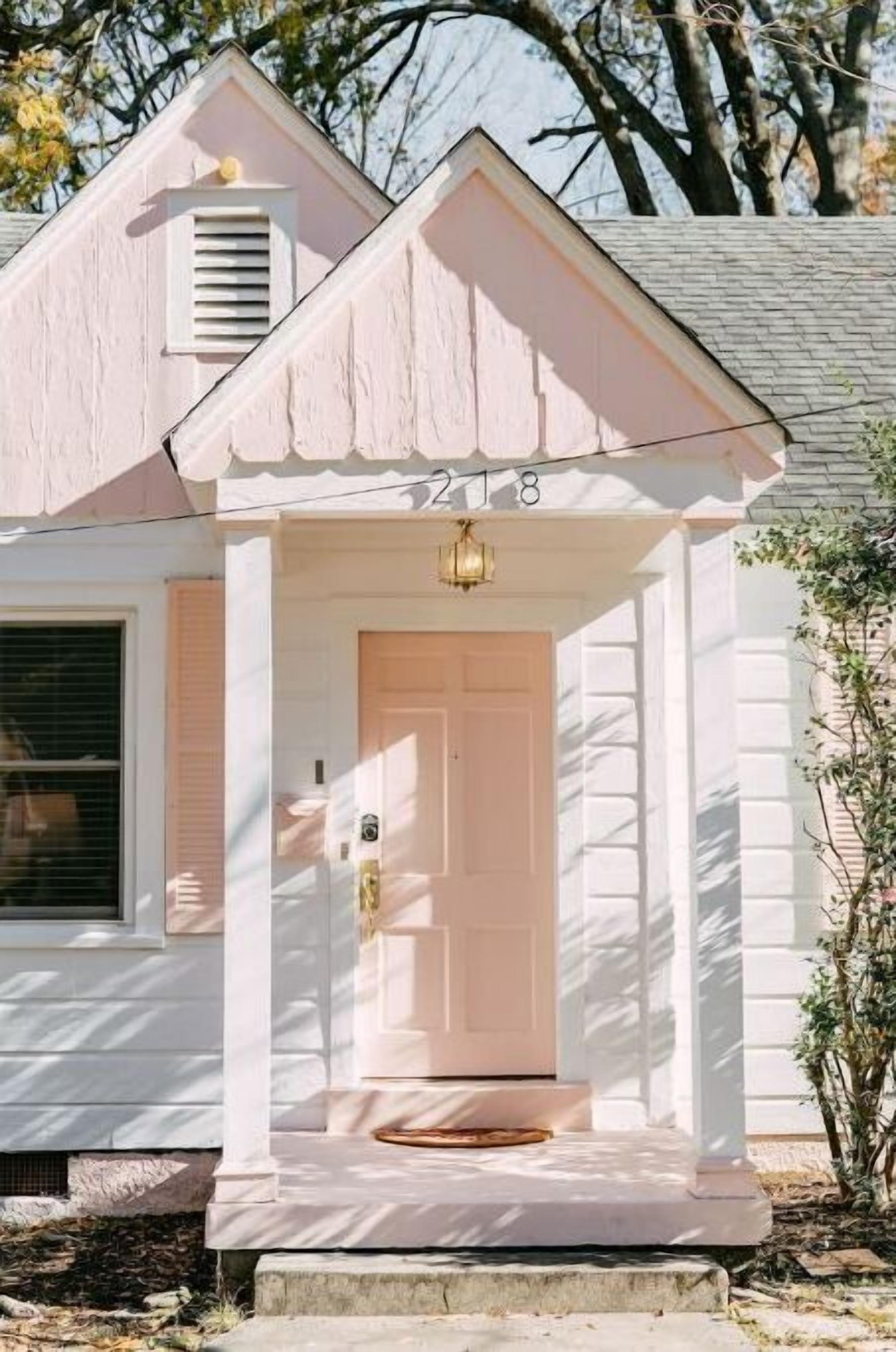 Een roze huis met een witte veranda, een deur en een klein raam.
