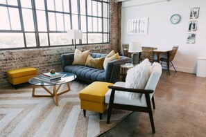 A living room with a sofa, ottoman, and coffee table, a dining area with chairs and a table, and a large window with a view. - Goldenrod by Pettigrew Adventures @ Crosstown (Memphis)