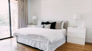 A bedroom with a large bed, white nightstands, and a view through a large window.