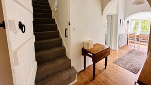 Uma escada com corrimão, uma mesa de madeira com um recipiente branco, e vista para área externa com mesa e cadeiras.