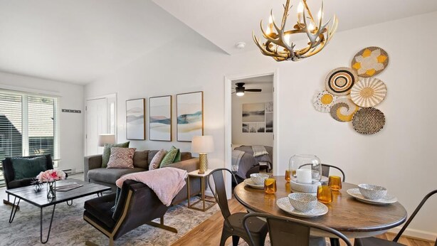 A modern living room with a dining area, featuring a chandelier, artwork, and a coffee table.