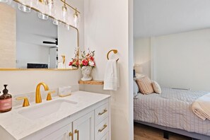 A modern bathroom with a white vanity, gold fixtures, and a large mirror.