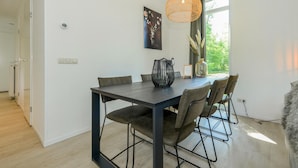 Un comedor moderno con una mesa de madera oscura, seis sillas y una lámpara colgante tejida.