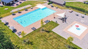 Vista aérea de un área de piscina con una pileta rectangular, rodeada de sillones y sombrillas, y un pequeño jardín con una decoración con forma de hongo.