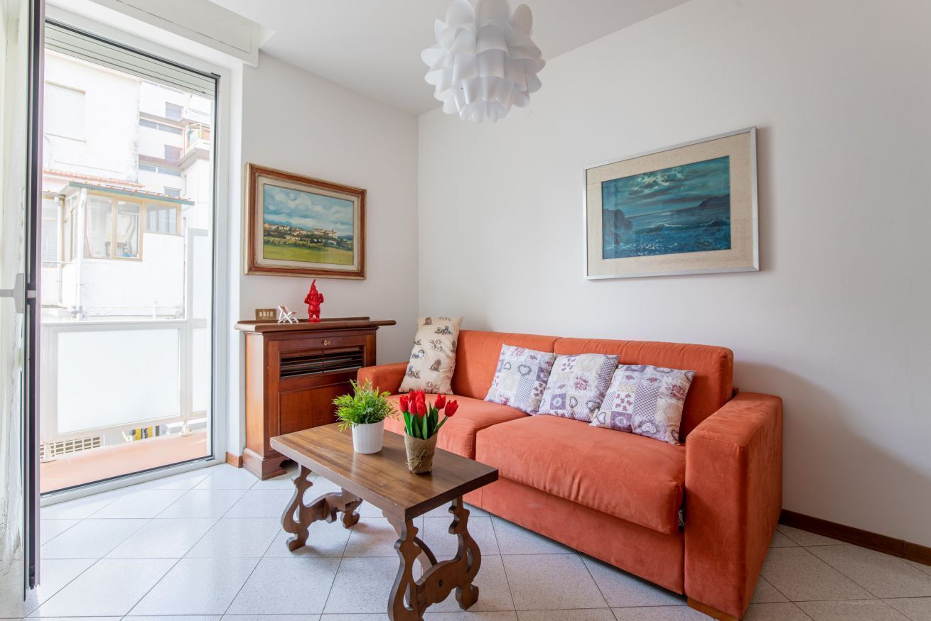 Una sala de estar con un sofá, una mesa de centro de madera, un cuadro y vistas a través de un ventanal corredero.