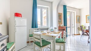 A compact kitchen with a white refrigerator, a dining table with chairs, and a view of a building through the window.