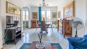 A living room with a TV, a dining table, chairs, a chandelier, and artwork on the walls.
