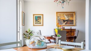 A dining area with a table set for four, a decorative glass dome over a pastry display, and two framed artworks on the wall.
