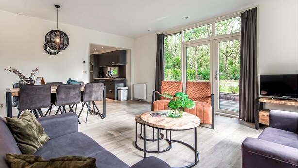 A modern living room with a sofa, a coffee table, and a TV. There is a dining area with chairs and a table. The room has large windows with a view of trees. - 3 bedroom gorgeous home in Zorgvlied (Zorgvlied)