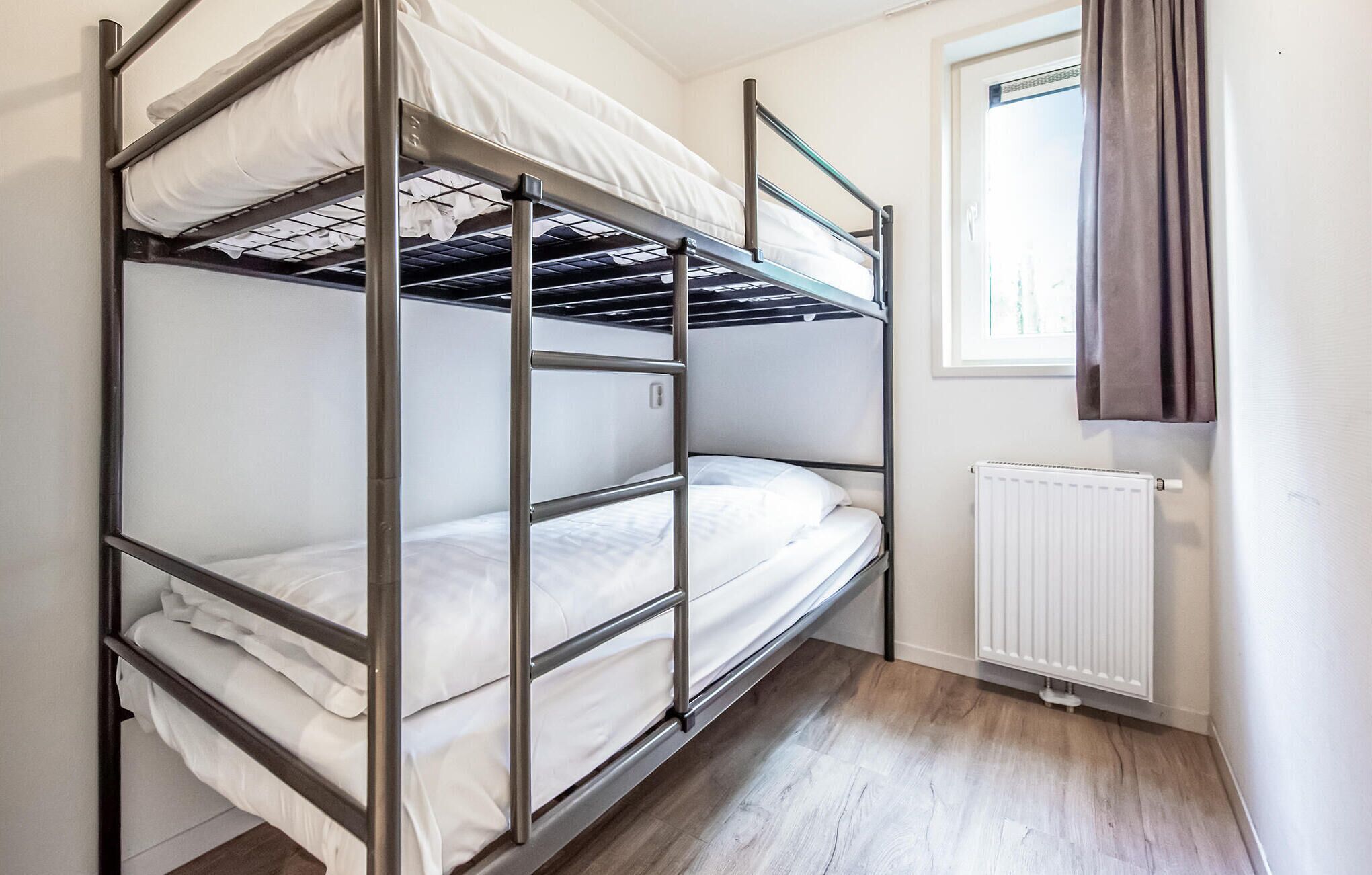 Une chambre avec un lit superposé, une fenêtre et un radiateur.