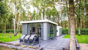 A modern, glass-walled structure with outdoor seating, surrounded by a lush garden and tall trees. - 3 bedroom gorgeous home in Zorgvlied (Zorgvlied)