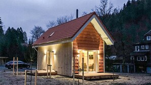 A small, single-story wooden cabin with a sloped roof, a porch, and a lit interior. - Awesome home in Clausthal-Zellerfeld with WiFi (Clausthal-Zellerfeld)