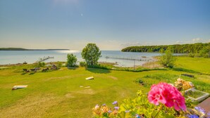 A grassy area with a dock extending into a lake, surrounded by trees and flowers. - Prairie-Style Home on Garden Bay w/ Deck + Hot Tub (Garden)