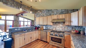 A spacious kitchen with wooden cabinets, a stone accent wall, and a large stove. - Prairie-Style Home on Garden Bay w/ Deck + Hot Tub (Garden)