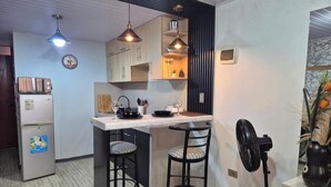 Une cuisine compacte dotée d’un îlot central, de luminaires suspendus, d’un réfrigérateur et d’un ventilateur.