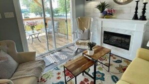 Una sala de estar con sofá, mesa de centro y chimenea. Hay una puerta corrediza de vidrio que da a un patio con mobiliario exterior.