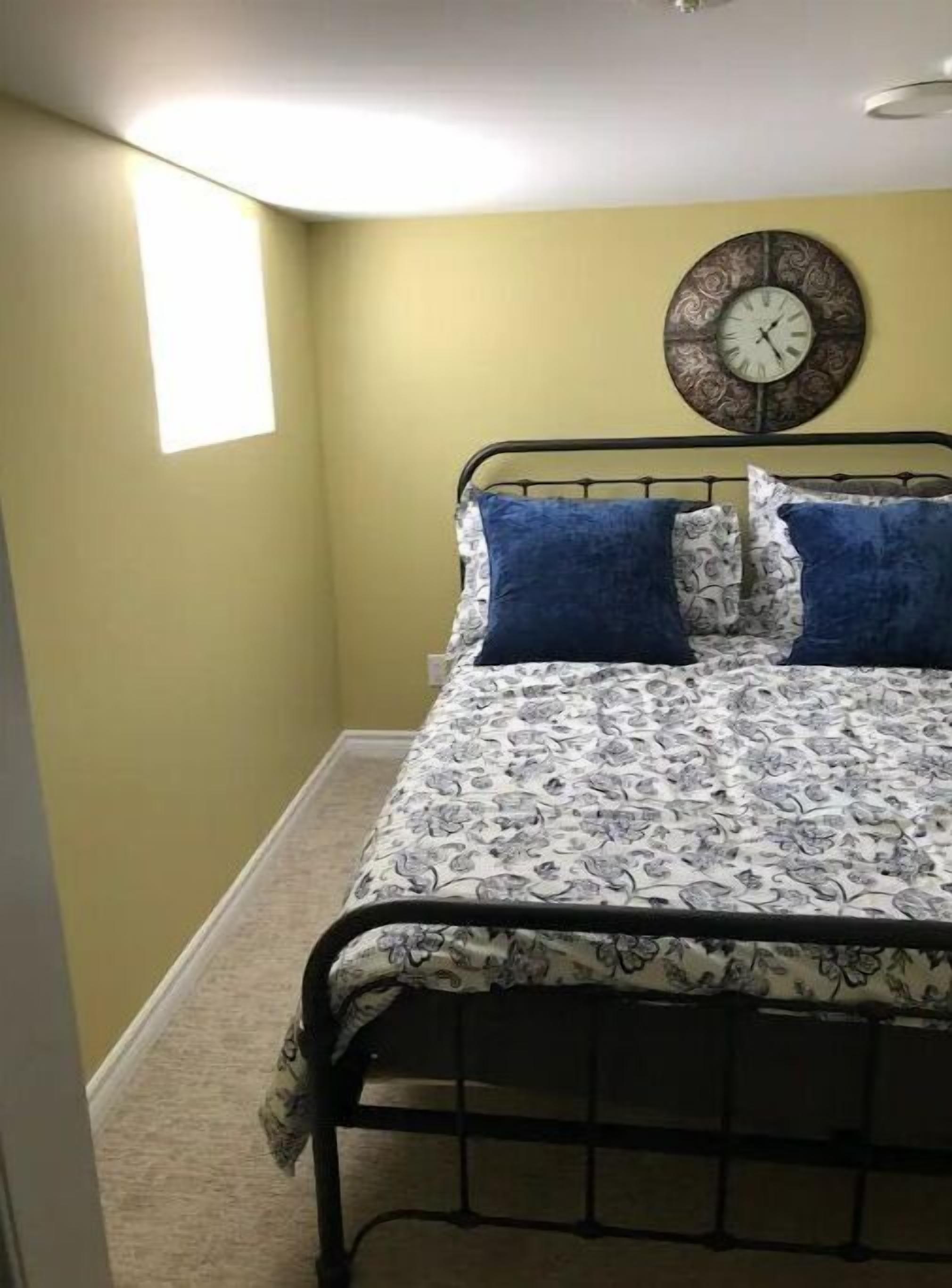A bedroom with a bed, a wall clock, and a window.