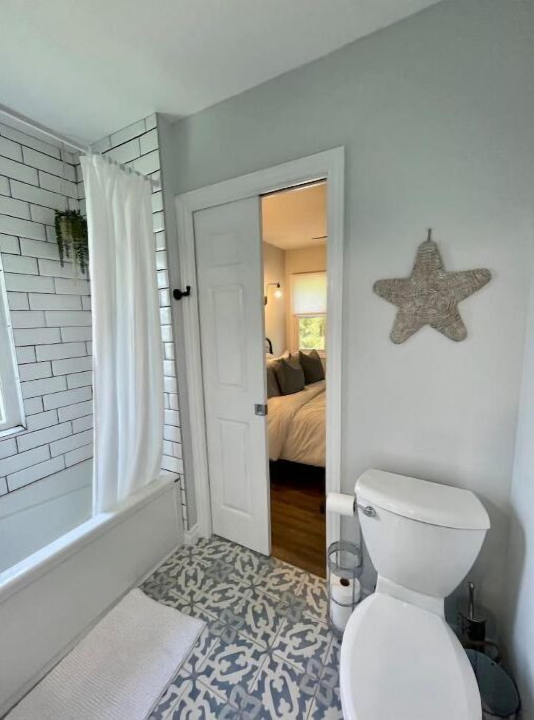 Un baño con inodoro blanco, piso estampado, cortina de ducha blanca y un adorno con forma de estrella en la pared.