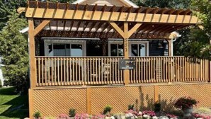 Una terraza de madera con un pérgola, un patio cubierto y un pequeño jardín con flores y rocas.