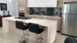 Una cocina moderna con una isla central, electrodomésticos de acero inoxidable y taburetes negros.