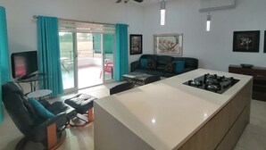 Una cocina moderna con una isla central, un comedor con mesa y sillas, un sofá y un ventilador de techo.