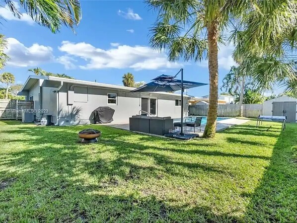 A modern house with a covered patio, a swimming pool, and a well-maintained lawn. - Lovely home with heated Pool a mile from the beach (Boca Raton)
