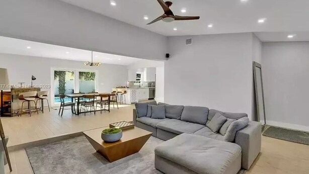 A spacious living area with a large grey sectional sofa, a wooden coffee table, and a ceiling fan. - Lovely home with heated Pool a mile from the beach (Boca Raton)