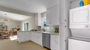 A modern kitchen with white cabinets, a dishwasher, and a large window providing natural light. - Lovely home with heated Pool a mile from the beach (Boca Raton)