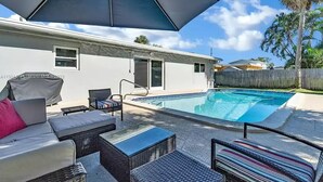 A poolside area with a covered seating area, a pool, and a wooden fence in the background. - Lovely home with heated Pool a mile from the beach (Boca Raton)