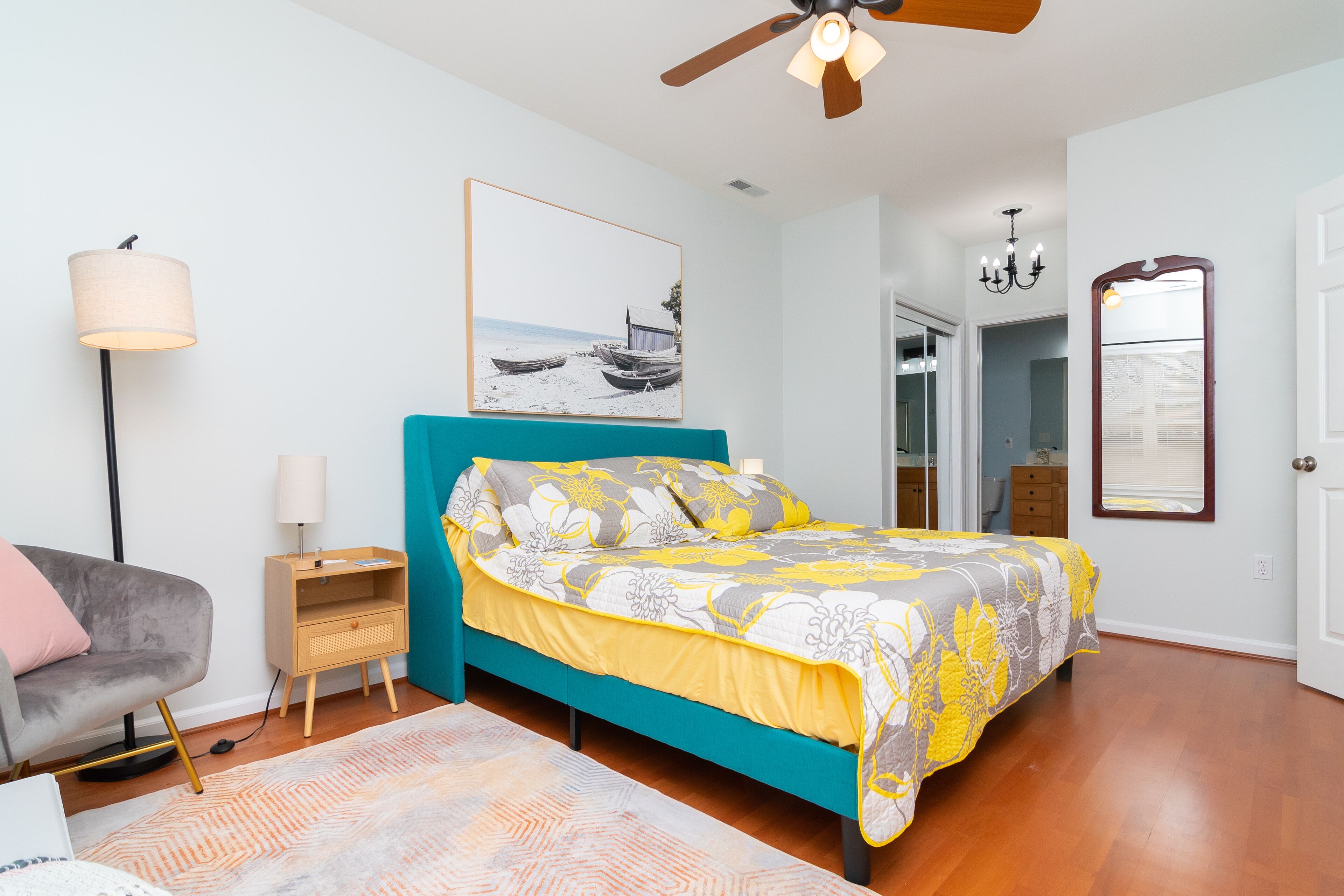 A bedroom with a bed, a nightstand, a lamp, a chair, a mirror, and a painting on the wall.