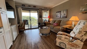 Un salon comprenant un canapé, un fauteuil, un pouf et un coin repas avec une table et des chaises.