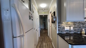 Une cuisine étroite avec des meubles blancs, un plan de travail noir et un plancher en bois.
