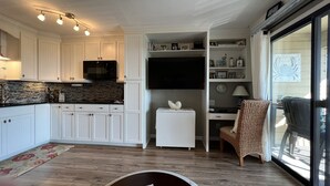 Une cuisine de taille réduite avec des meubles blancs, un micro-ondes noir et un pare-feu en carreaux.