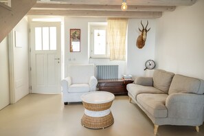 A living room with a white chair, a grey sofa, a wicker coffee table, a mounted animal head, and a wall clock.