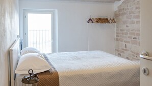 A bedroom with a bed, a window, a door, and a brick wall. -  A26 - Poggio, sky-land with breathtaking sea view (Ancona)
