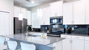 A modern kitchen with white cabinets, stainless steel appliances, and a central island with bar stools. - Superhero Game Room • Mickey Room • Pool & Spa • 4 Miles to Disney (Kissimmee)
