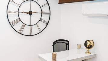 Ein Zimmer mit weißem Schreibtisch, schwarzem Bürostuhl, großer Wanduhr und kleinem Globus an der Wand.