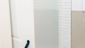Une salle de bain avec une douche à parois de verre, des murs recouverts de carreaux blancs et un sol de couleur beige.