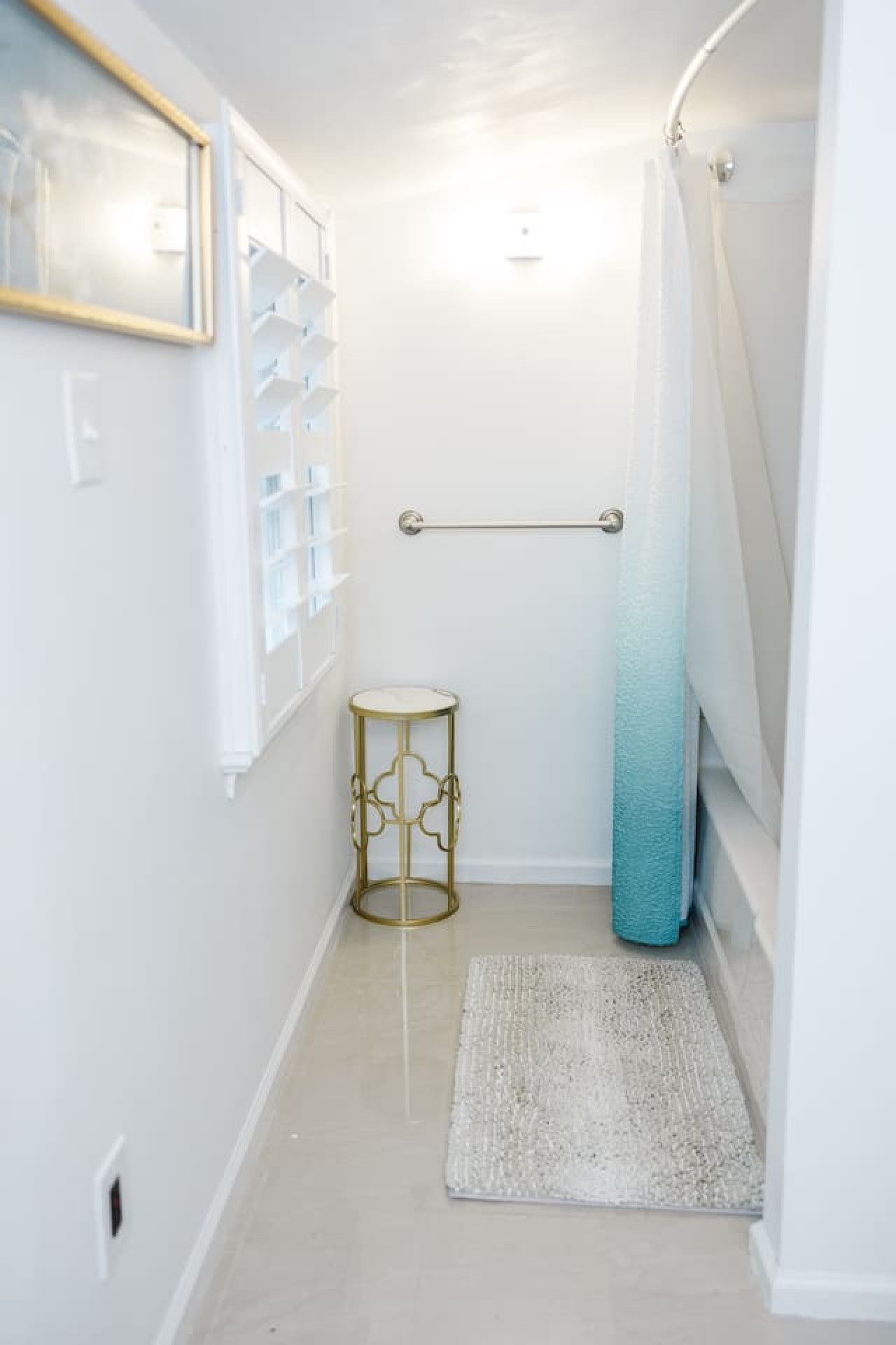 A narrow hallway with a white floor, a small round table, a blue towel, and a shower curtain.