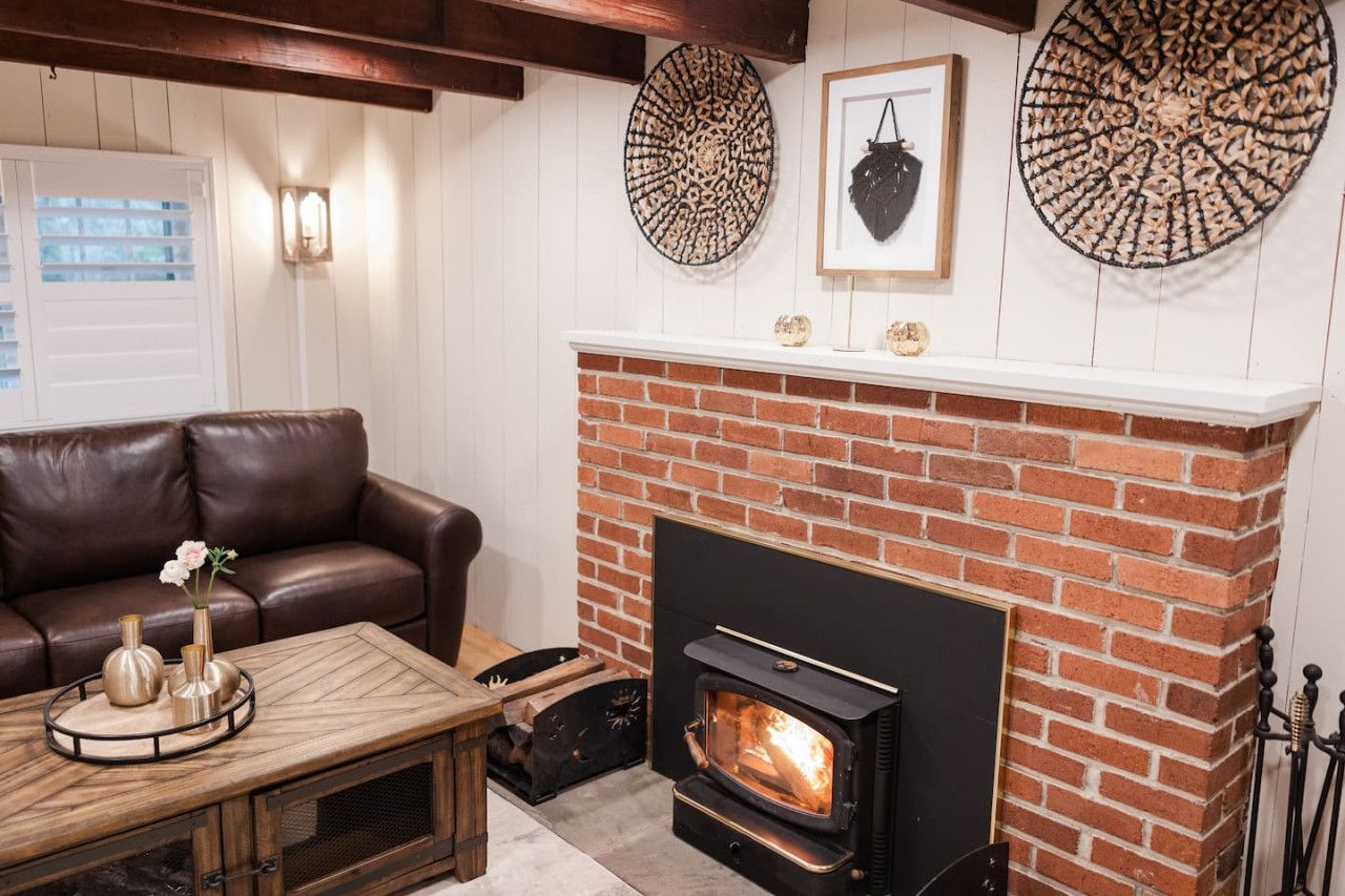 Una sala de estar acogedora con chimenea de ladrillo, sofá de cuero y decoración mural.
