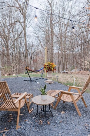 An outdoor seating area with wicker chairs and a small round table, surrounded by a gravel path and a hammock.