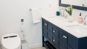 A modern bathroom with a white toilet, a trash bin, a sink with a mirror, and a small plant on the counter. - Cowry Acres - The First House Villa w Hot Tub (New Hope)