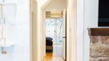 Ein schmaler Korridor mit Holzboden führt zu einem Zimmer mit Bett und Fenster.