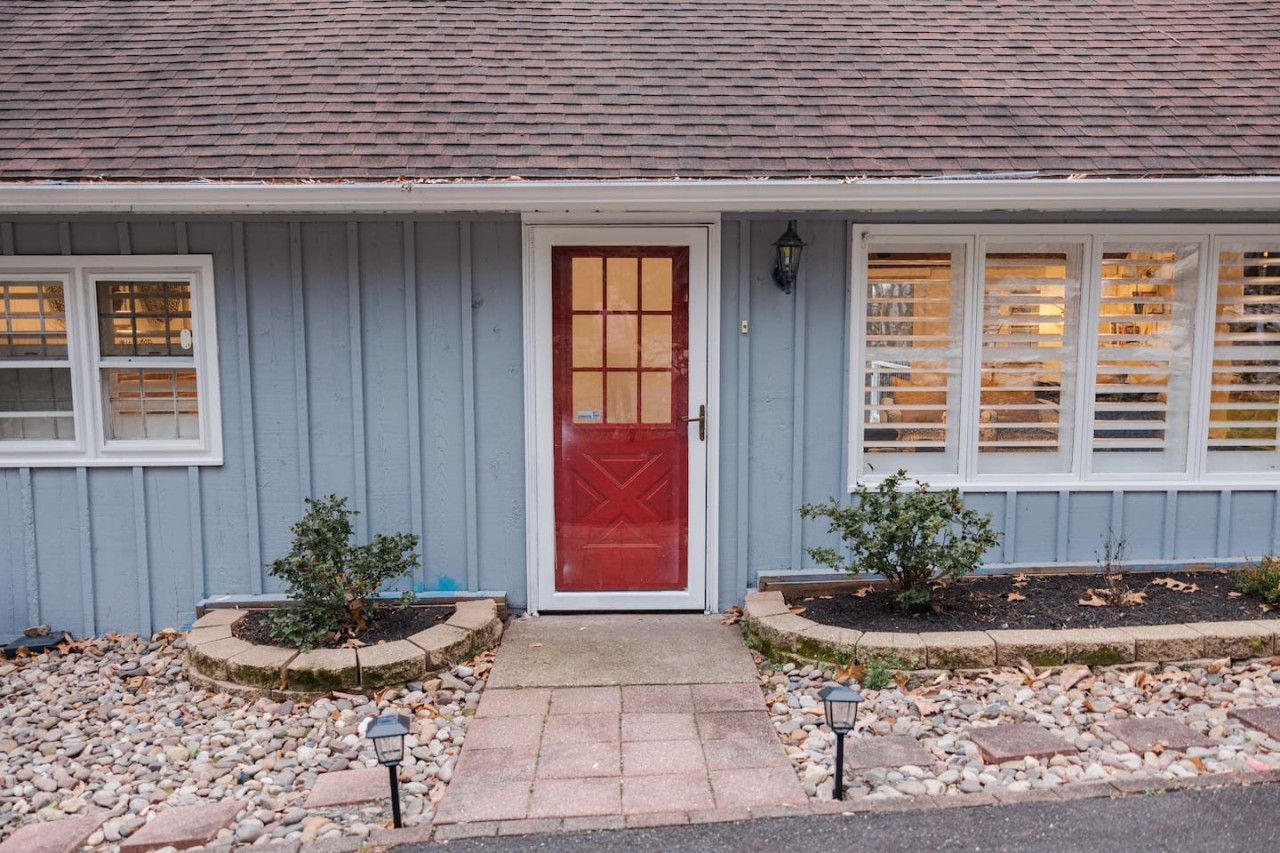 A house with a red door, white-framed windows, and a grey siding exterior.