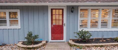 Une maison avec une porte rouge, des fenêtres à cadre blanc et un revêtement extérieur gris.